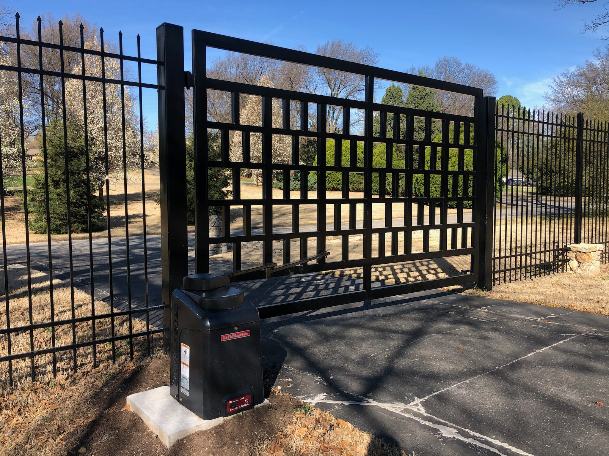 Black geometric ornamental swing gate with a LiftMaster operator mounted on a concrete pad.