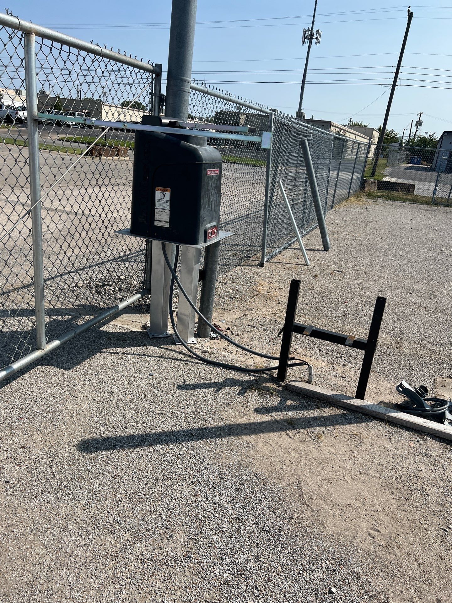 LiftMaster operator on a steel pedestal beside a commercial chain-link gate during installation work.